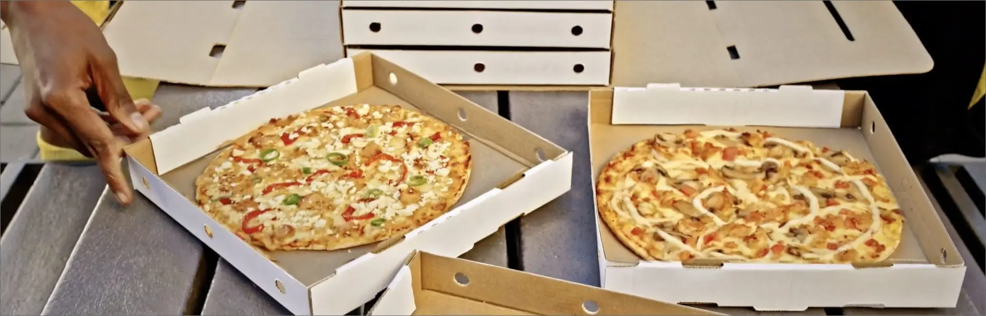 Two open takeout pizza boxes filled with freshly baked pizzas featuring peppers, mushrooms, and melted cheese.